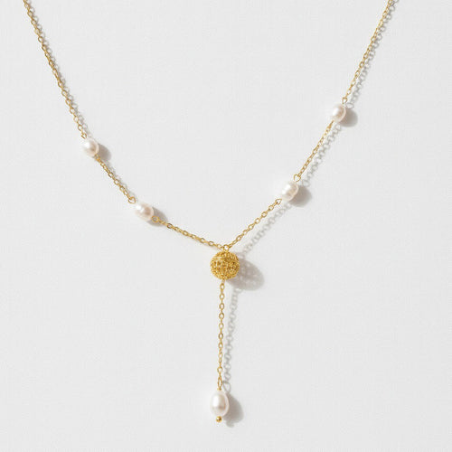 A delicate gold Y-necklace featuring small white pearls spaced along the chain and a textured gold circular pendant at the center, with a longer drop chain ending in a larger pearl, shown on a light gray background.